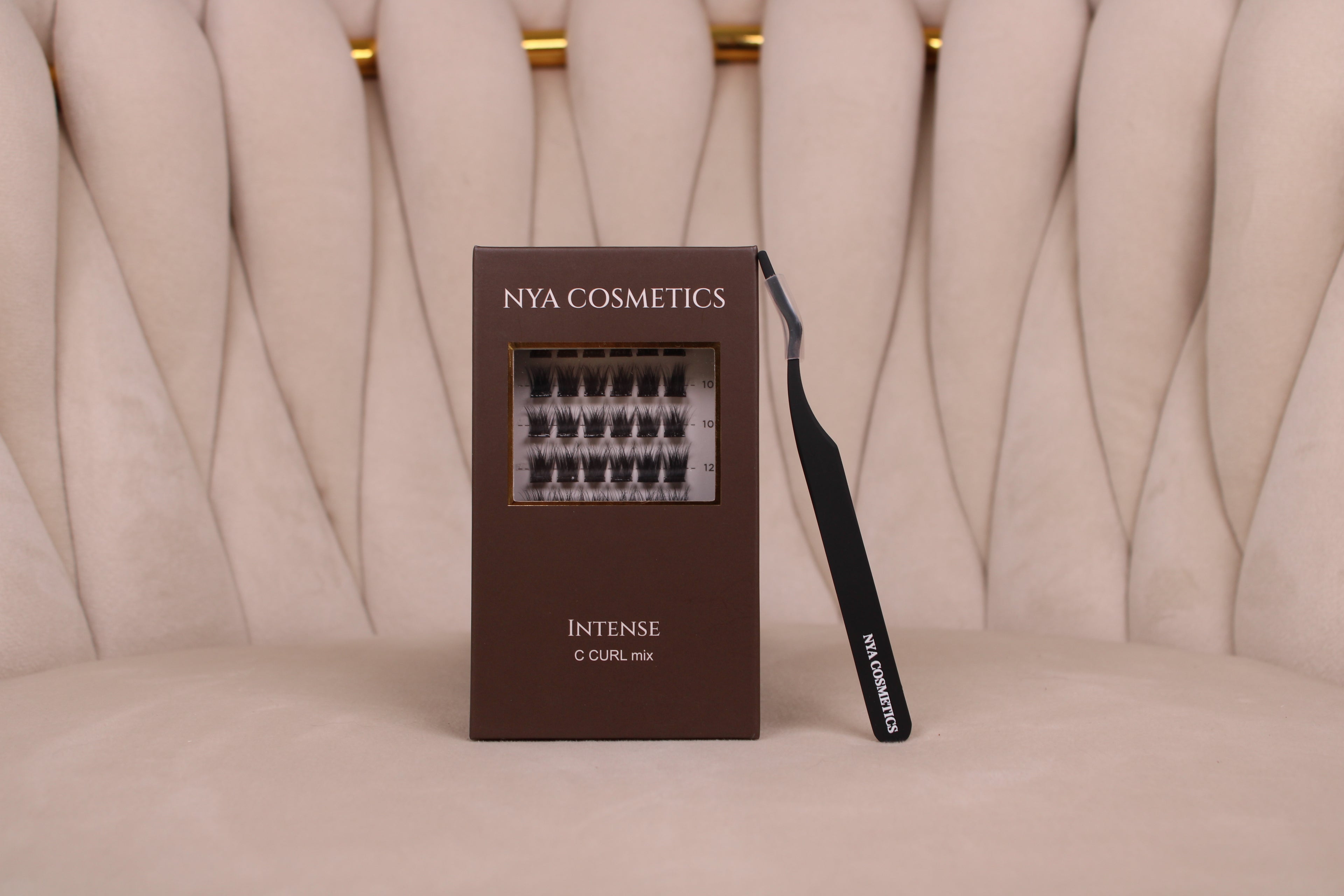 Kit de démarrage faux cils auto-adhésifs NYA Cosmetics gamme Intense C Curl mix avec la pince de précision NYA Cosmetics noire sur fauteuil capitonné beige doré nouvelle collection 2026