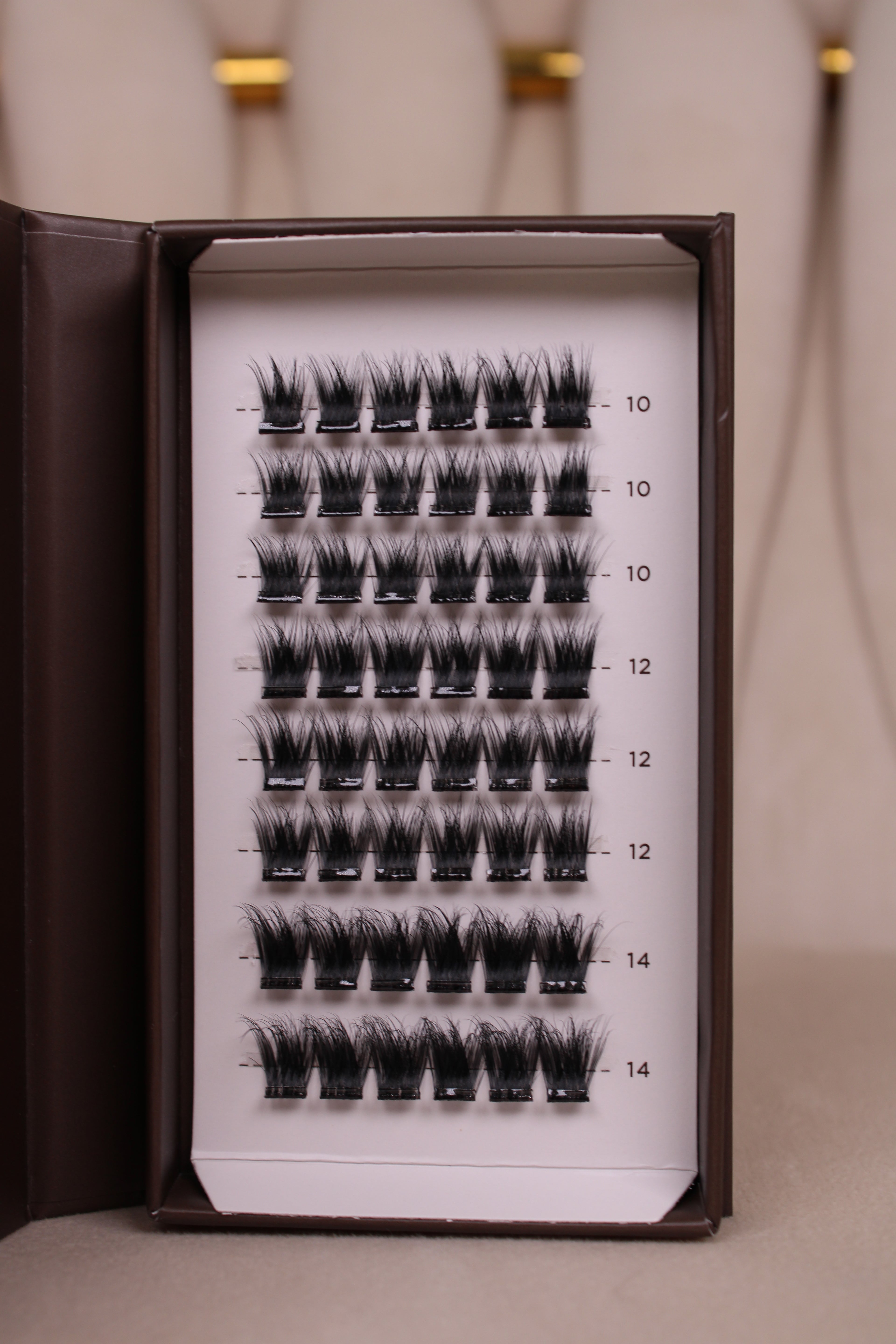 Plateau de faux cils auto-adhésifs NYA Intense ouvert montrant les clusters volumineux en longueurs 10mm 12mm et 14mm sur fond beige