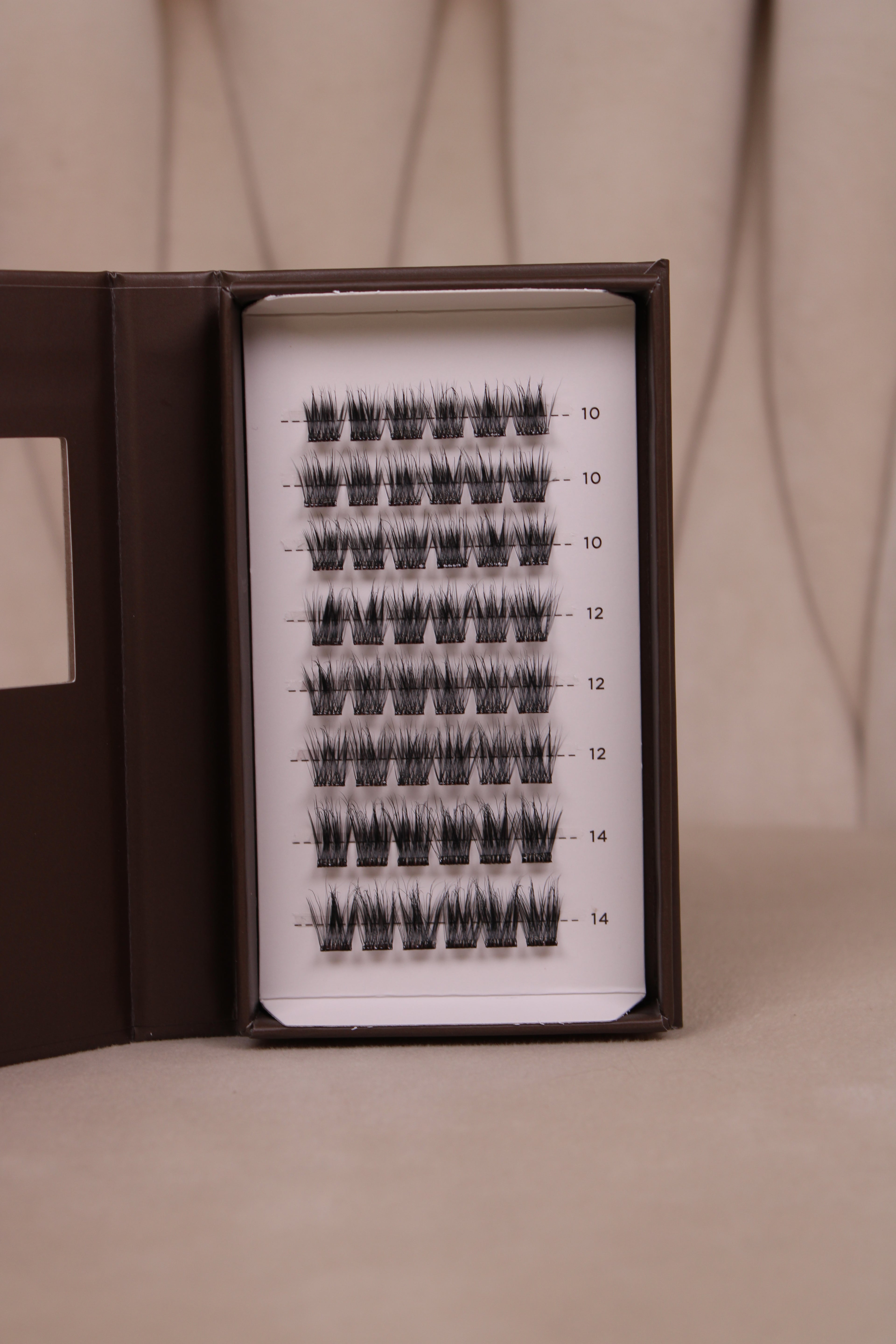 Plateau de faux cils auto-adhésifs NYA Soft ouvert montrant les clusters en longueurs 10mm 12mm et 14mm sur fond beige